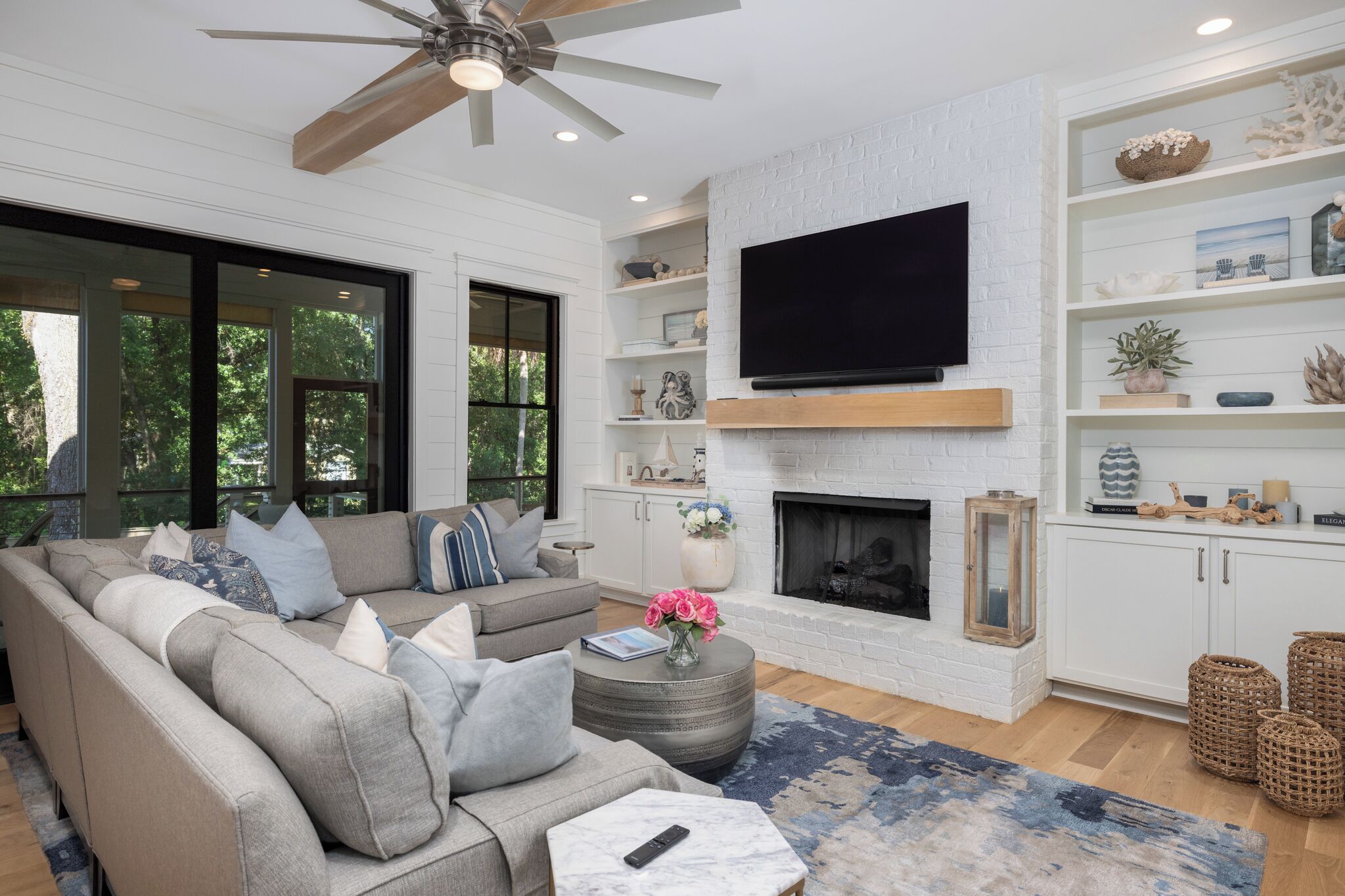 A modern living room with a fireplace, a ceiling fan, and a large TV mounted on the wall.