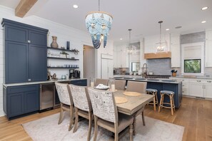 A modern kitchen with a central island, pendant lighting, and a dining area with chairs and a table. - Stay @ Isle of Coladas (Isle of Palms)