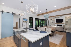 A modern kitchen with a central island, pendant lights, and a dining area with a table and chairs. - Stay @ Isle of Coladas (Isle of Palms)