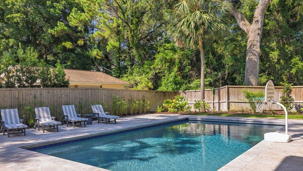 A rectangular swimming pool with a tiled edge, surrounded by lounge chairs and a wooden fence. - Stay @ Isle of Coladas (Isle of Palms)