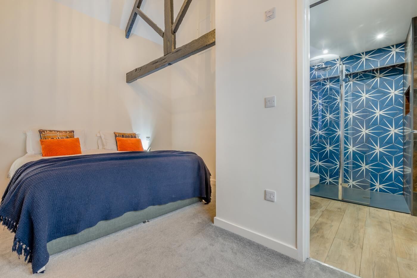 A bedroom with a bed, a nightstand, and a bathroom with a shower and patterned tiles.