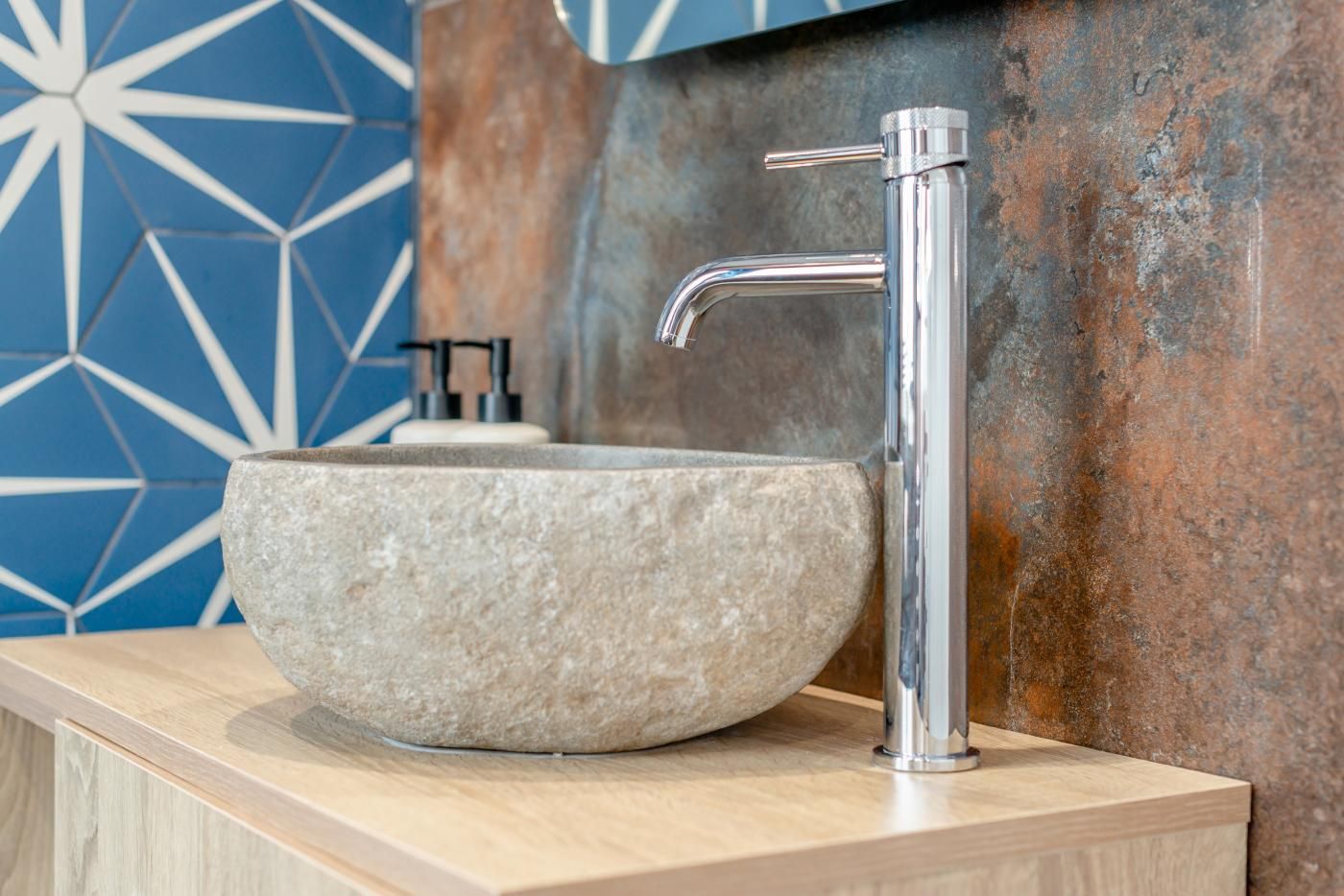 Une salle de bain avec un lavabo en pierre, un robinet chromé et un mur orné d’un motif géométrique.