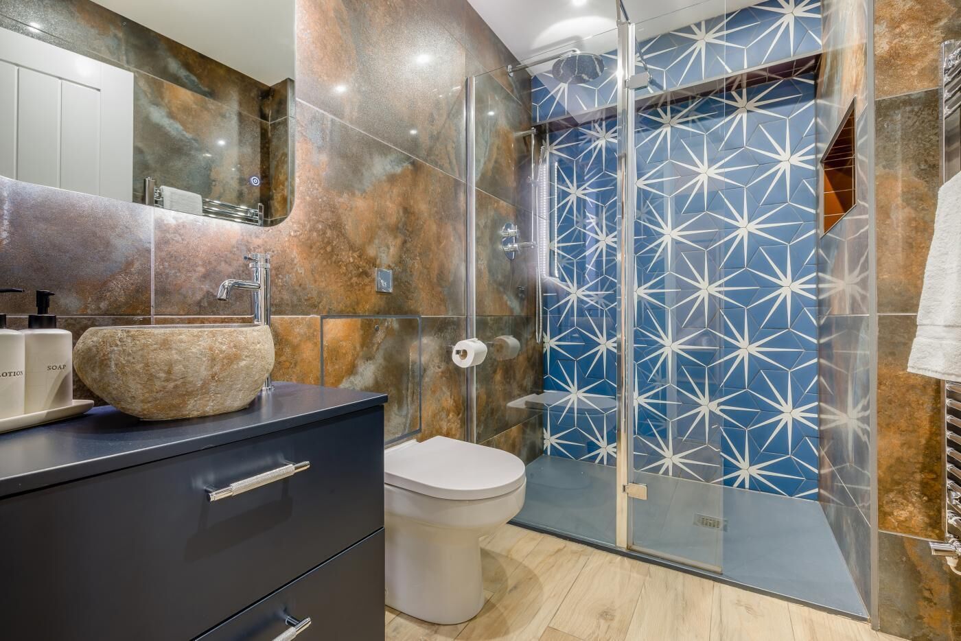 Un baño moderno con un lavabo de piedra, un inodoro y una ducha con paredes de azulejos geométricos.