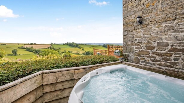 A hot tub with a stone wall and a view of green fields. - 1 Bed in Welshpool (oc-381818) (Welshpool)