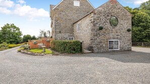 A stone building with a gravel driveway and a fenced garden area. - 1 Bed in Welshpool (oc-381818) (Welshpool)