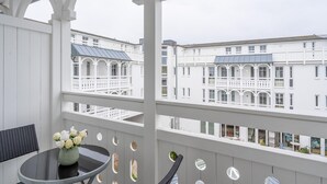 Ein Balkon mit Tisch und Stühlen, eine Vase mit Blumen und Blick auf weiße Häuser mit Balkonen.