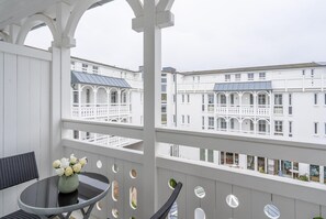 A balcony with a table and chairs, a vase with flowers, and a view of white buildings with balconies. - Ostseeurlaub fur 2 - Ferienwohnung in Sellin mit Balkon (Sellin)