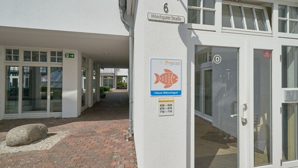 Ein Gebäude mit einem Schild, das 'Mönchgut Straße' und ein Fischsymbol zeigt, was auf einen Ort im Zusammenhang mit Fischerei oder Meeresfrüchten hindeutet.