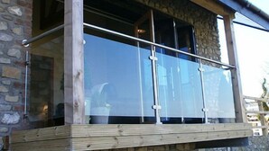 Ein Steinhaus mit einem Balkon, der eine Glastrennwand und Holzbalken besitzt.