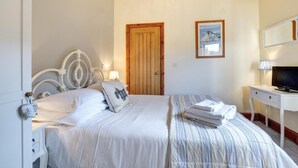 Ein ordentlich eingerichtetes Schlafzimmer mit Bett, Nachttisch, Lampe und Fernseher.