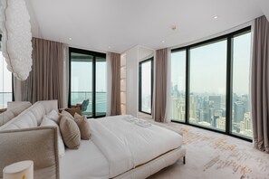 Ein modernes Schlafzimmer mit einem großen Bett, Blick auf die Stadt und einem Hochhaus im Hintergrund.