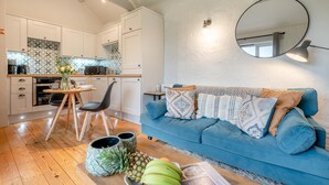 Eine moderne Küche mit weißen Schränken, ein Essbereich mit Tisch und Stühlen sowie ein blaues Sofa mit gemusterten Kissen.
