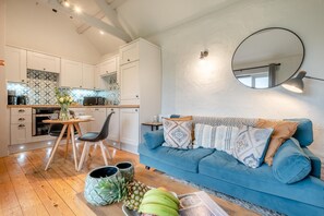 Eine moderne Küche mit weißen Schränken, ein Essbereich mit Tisch und Stühlen sowie ein blaues Sofa mit gemusterten Kissen.