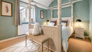 Ein Bett mit Baldachin, eine Sitzbank, ein Nachttisch und ein Fenster mit Vorhängen.