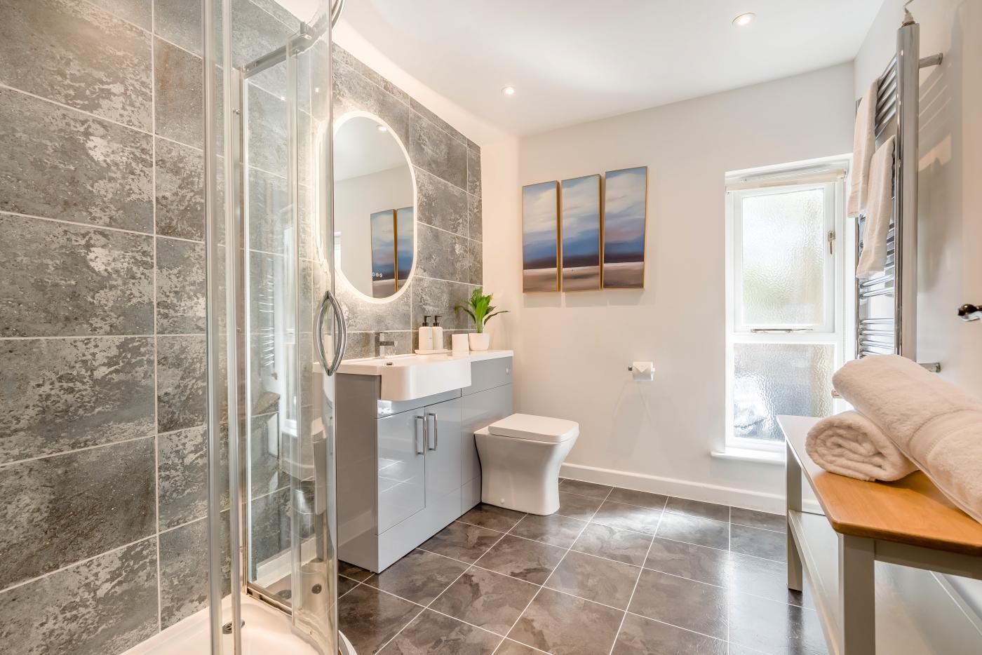Ein modernes Badezimmer mit Duschkabine aus Glas, Waschtisch mit Spiegel, Toilette und Fenster.