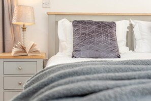 A neatly made bed with a gray blanket, a bedside lamp, and an open book on a nightstand. - 1 Bed in St. Gennys (oc-s34628) (Crackington Haven)