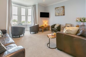 A living room with leather sofas, a coffee table, a TV, and a painting on the wall. - 3 Bed in Porthleven (oc-bayvil) (Porthleven)