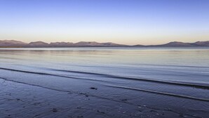 Ein ruhiger Strand mit sanften Wellen, blauem Himmel und fernen Bergen.