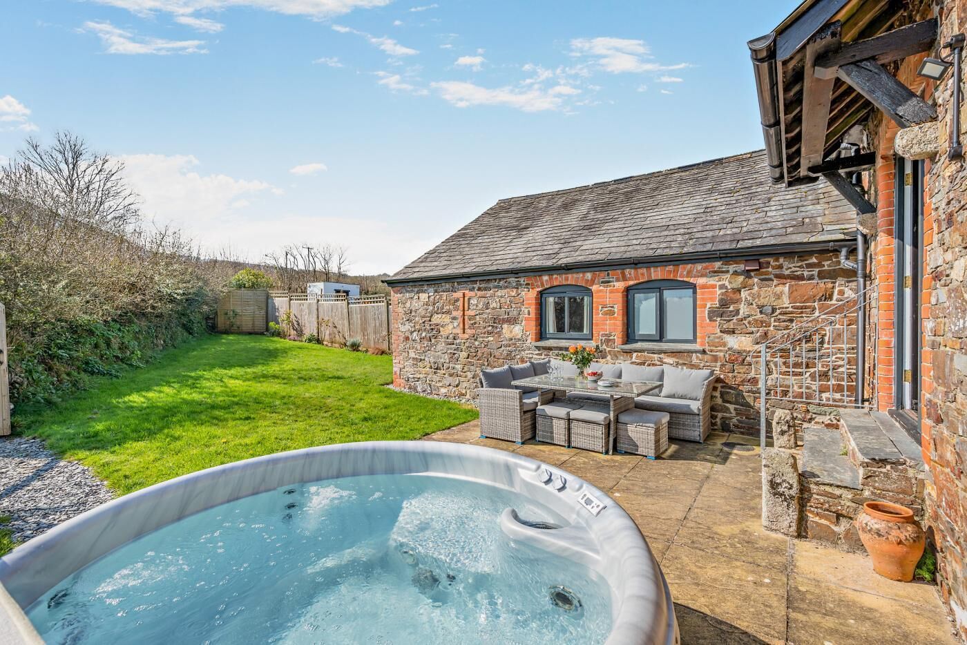 A stone building with a hot tub, outdoor seating, and a grassy yard.