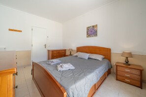 A bedroom with a bed, bedside tables, a wooden dresser, and a door. - Casa Cruzeiro Praia da Rocha (Portimão)