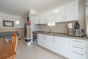 A modern kitchen with white cabinets, a stainless steel sink, a built-in oven, and a coffee maker. - Casa Cruzeiro Praia da Rocha (Portimão)