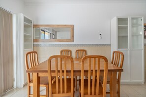 A dining area with a wooden table and chairs, a mirror above the table, and a white cabinet with glass doors. - Casa Cruzeiro Praia da Rocha (Portimão)
