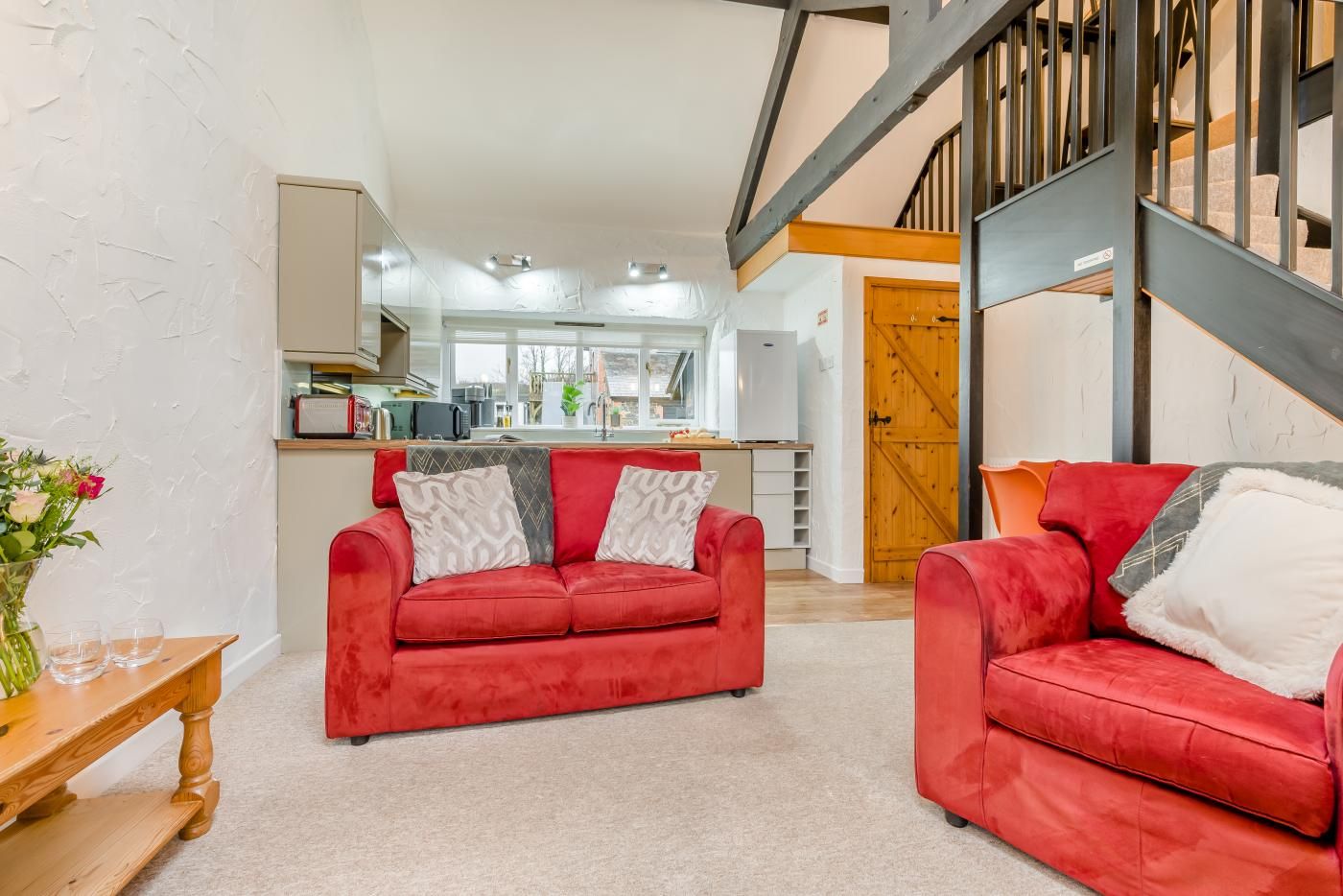 A spacious living area with a red sofa set, a wooden coffee table, and a kitchen in the background.