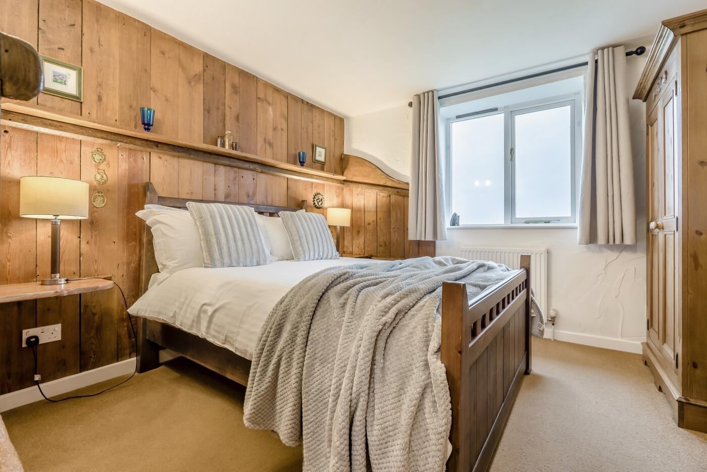 Un dormitorio con cama de madera, lámparas de noche, una ventana con cortinas y un radiador.