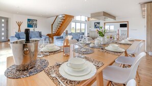 En rummelig spiseafdeling med et højt til loftet, en trappe og et moderne køkken i baggrunden.
