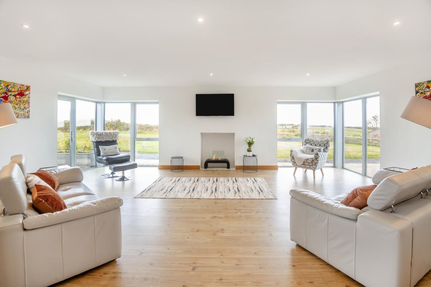 A spacious living room with a fireplace, two sofas, a TV, and large windows offering a view of the outdoors.