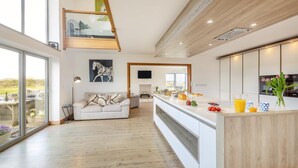 Et moderne køkken med en central ø, et spiseområde med en sofa og et stort vindue med udsigt til en have.