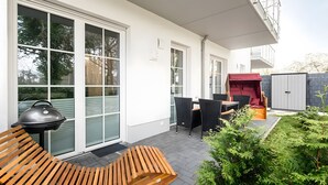 Een terras met een barbecue, een houten bank, een buitentafel, stoelen en een rode speeltent.
