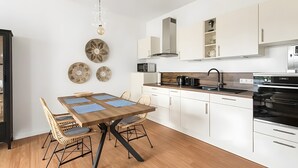 Een moderne keuken met witte kasten, een houten eettafel, rieten stoelen en een ingebouwde oven.