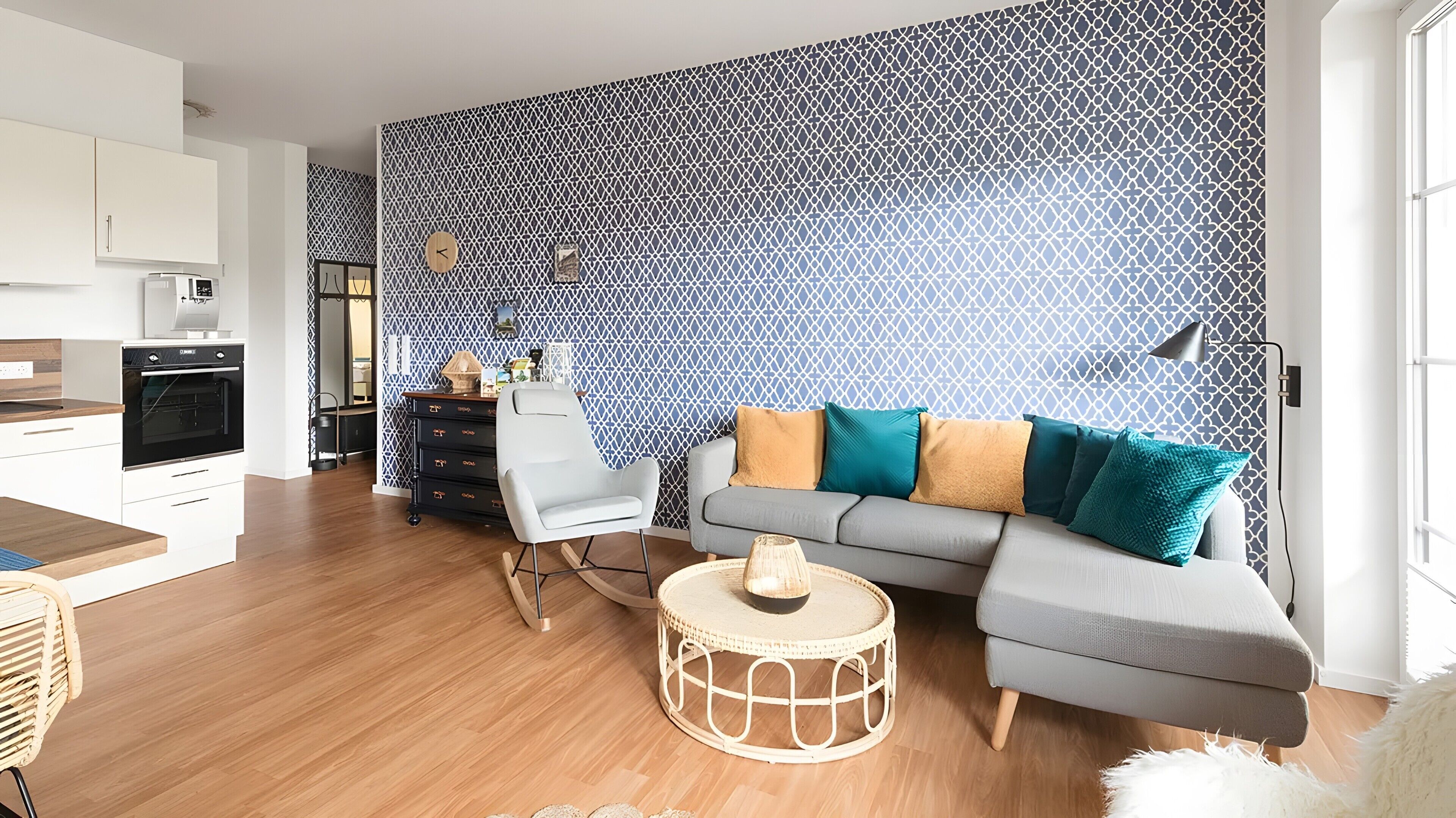 A modern living room with a grey sofa, a round coffee table, a white chair, and a patterned wall.