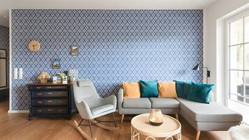 Uma sala de estar com parede estampada, um sofá, uma poltrona de balanço, uma mesinha lateral e um relógio.