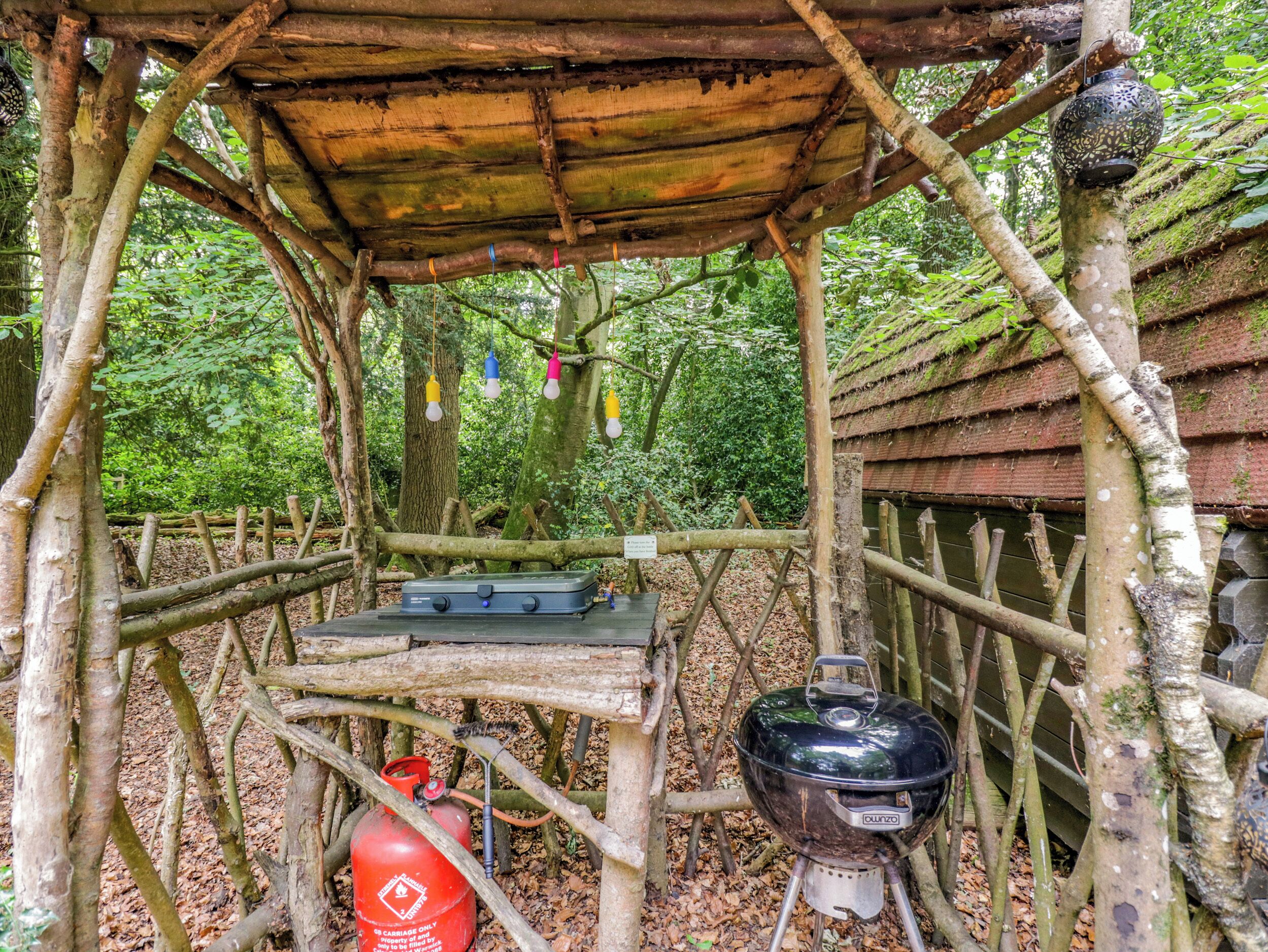 Ein rustikaler Kochbereich im Freien mit Grill, Gasflasche und klappbarem Tisch.