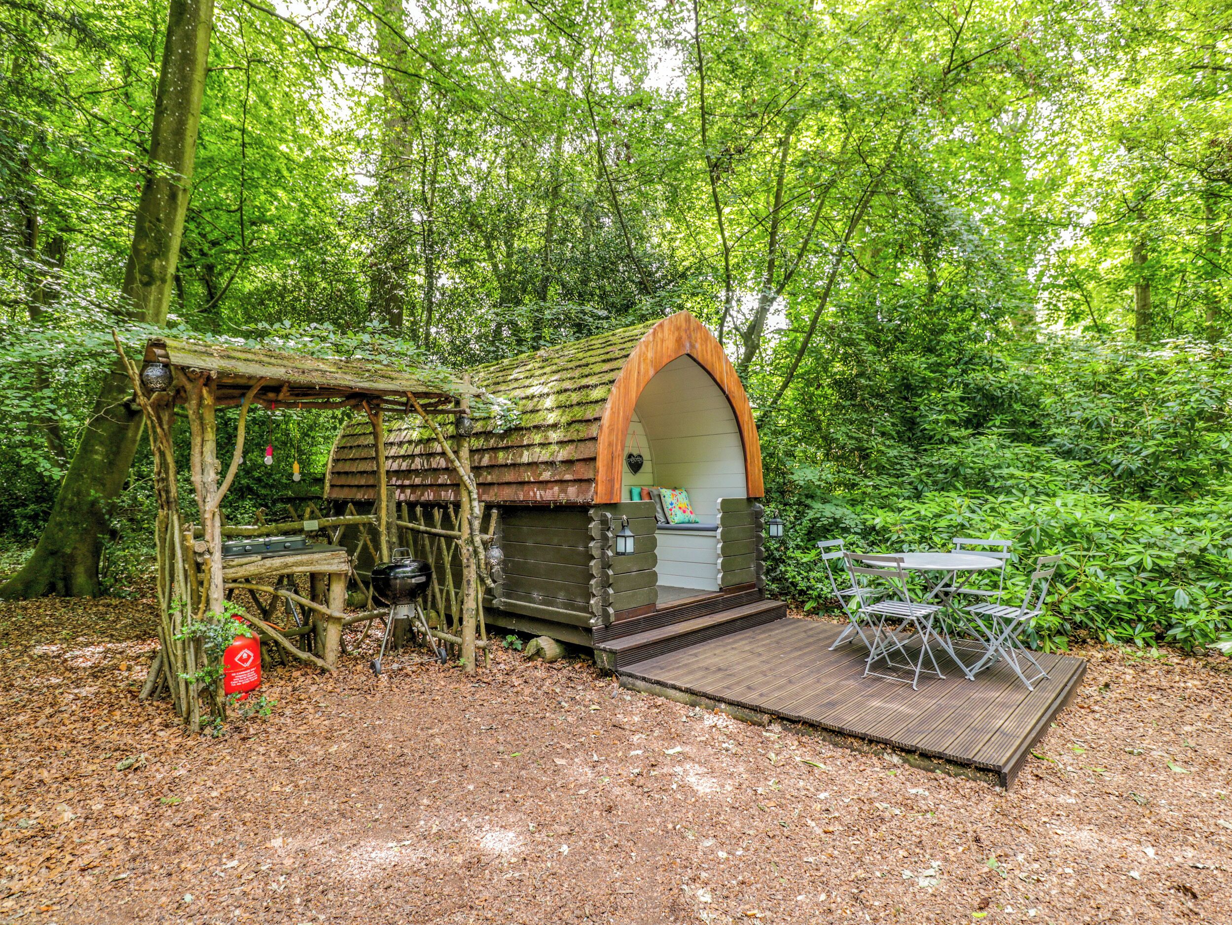 A rustic wooden cabin with a bench and a table in a forested area.