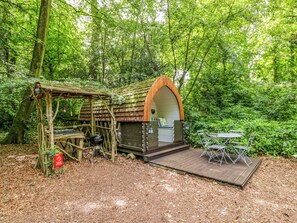 Une cabane en bois rustique, avec un banc et une table, située dans une zone boisée.