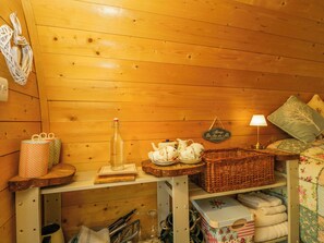 A cozy cabin interior with wooden walls, a small table with tea set, a lamp, and a basket. - Daisy Glamping Pod (Newbury)