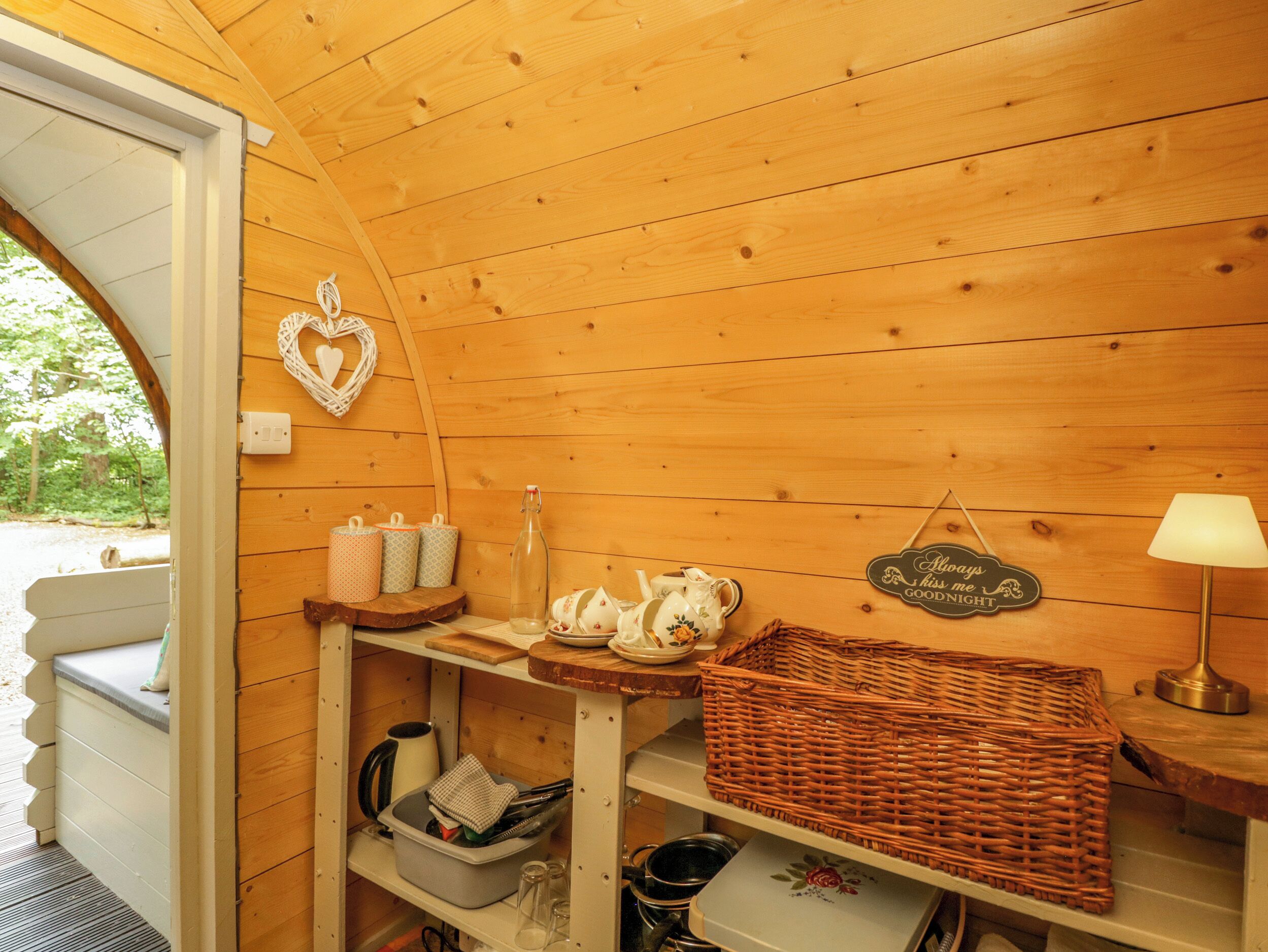 A cozy cabin interior with wooden walls, a heart-shaped decoration, a sign, a lamp, and a wicker basket.