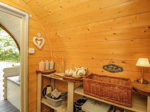 A cozy cabin interior with wooden walls, a heart-shaped decoration, a sign, a lamp, and a wicker basket. - Daisy Glamping Pod (Newbury)