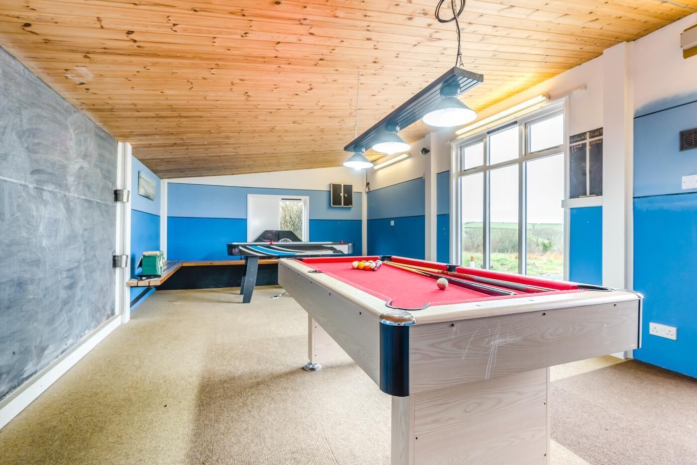 A pool table in a room with blue walls, a wooden ceiling, and large windows.