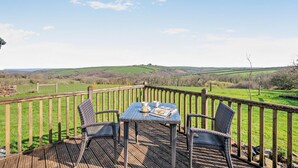 A wooden deck with wicker chairs and a table, overlooking a green landscape. - 1 Bed in St. Gennys (oc-v34634) (Crackington Haven)