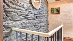 Un escalier avec un mur en pierre, une horloge et un tableau encadré accroché au mur.