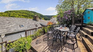 Une terrasse dotée de mobilier d’extérieur, offrant une vue sur une montagne et donnant sur un bâtiment bleu.