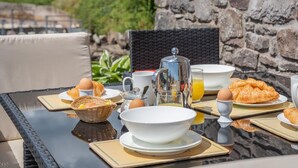 Frühstücksaufteilung mit Croissants, Eiern und Orangensaft auf einem Glastisch vor einer Wand aus Stein.