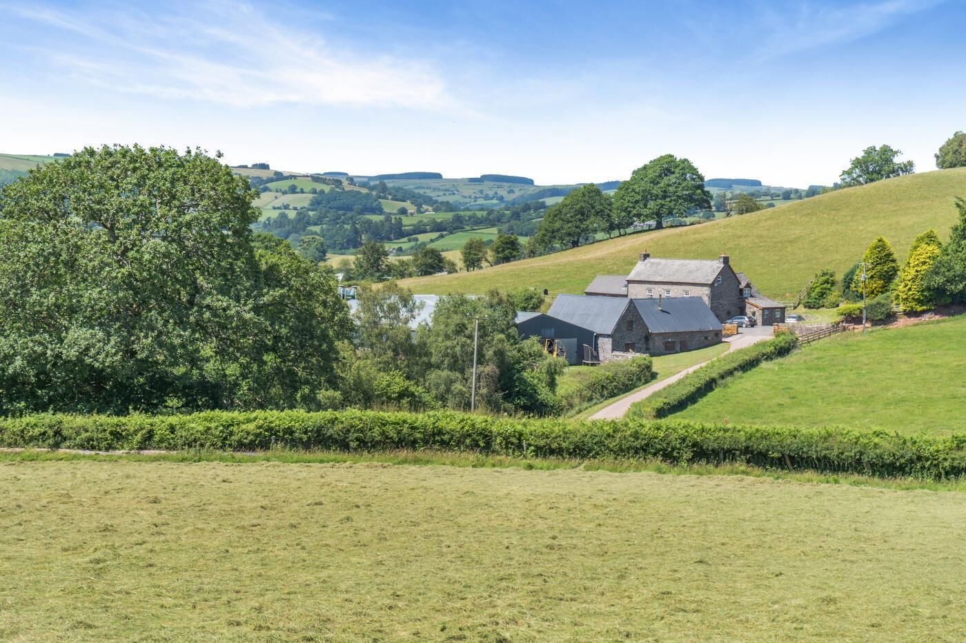 A rural landscape with a stone house, a path leading to it, and rolling hills in the background.
