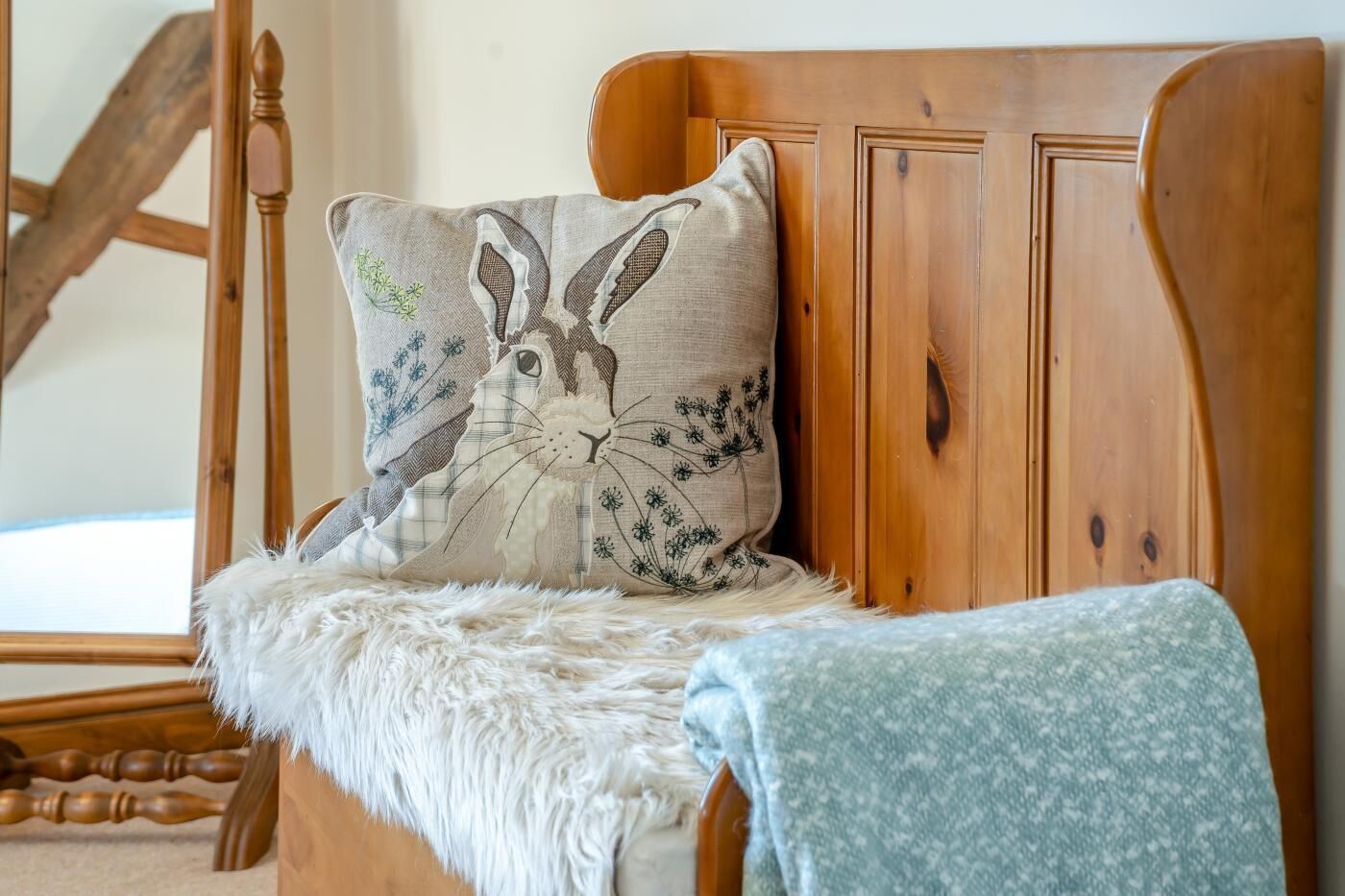 A wooden bed with a white fluffy throw blanket and a pillow with a rabbit design.