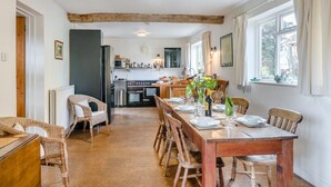 A dining area with a wooden table set for four, flanked by wicker chairs, leading to a kitchen with modern appliances. - 3 Bed in Awre (oc-s34503) (Awre)