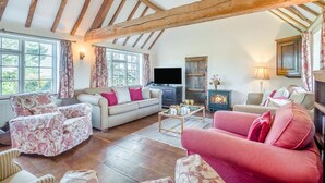 A cozy living room with a high ceiling, a fireplace, a television, and floral-patterned furniture. - 3 Bed in Awre (oc-s34503) (Awre)